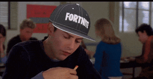 a man wearing a hat that says fortnite is sitting at a table with a pencil in his hand .