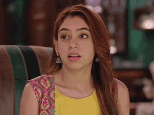 a woman in a yellow top is sitting on a couch and making a funny face