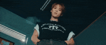 a young man wearing a black t-shirt with a cross on it is standing in a dark room .