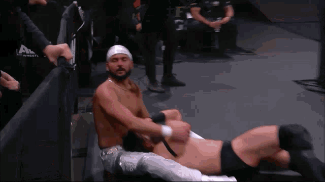 a wrestler with a bandage on his head is laying on the floor with another wrestler