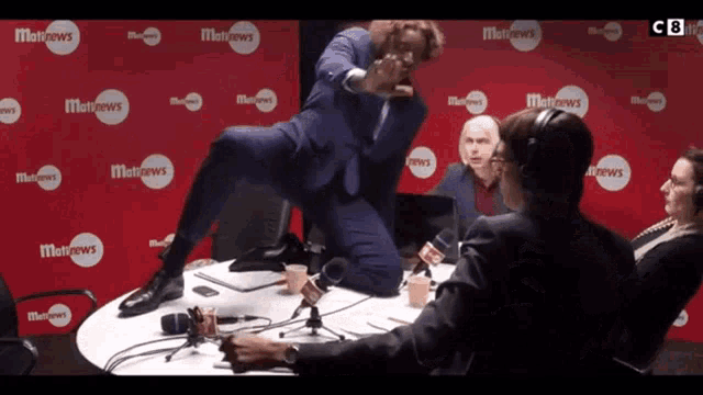 a man in a suit is jumping over a table in front of a wall that says matnews