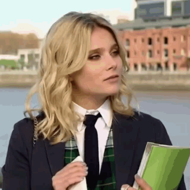 a woman wearing a suit and tie is holding a green book .
