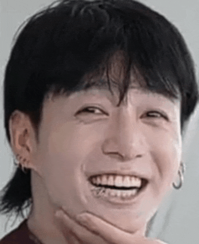 a close up of a person 's face with their hand on their chin and a smile on their face .