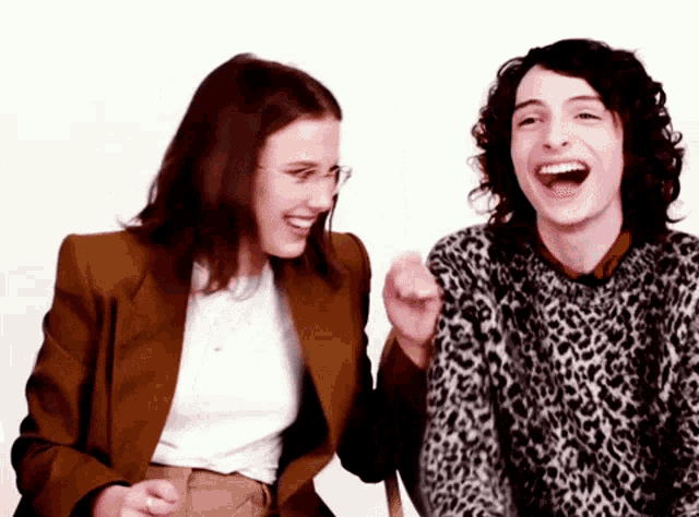 a man in a leopard print sweater and a woman in a brown jacket are laughing together