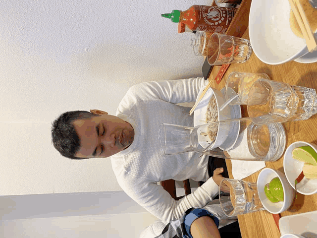 a man sitting at a table with a bottle of sriracha sauce