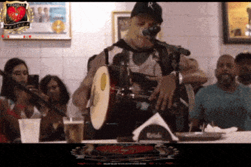 a man playing a drum and singing into a microphone in front of a sign that says primeiro