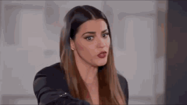a woman in a black jacket is making a funny face while holding her hand out .