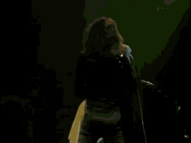 a man in a white robe is playing a guitar on stage while another man stands behind him .
