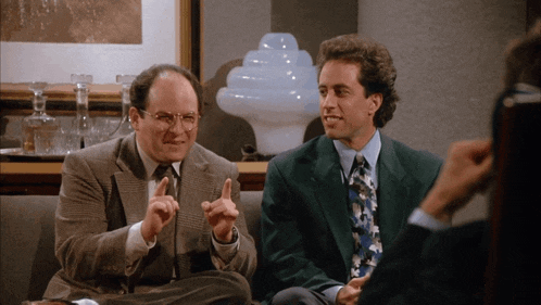 two men are sitting on a couch and one is pointing