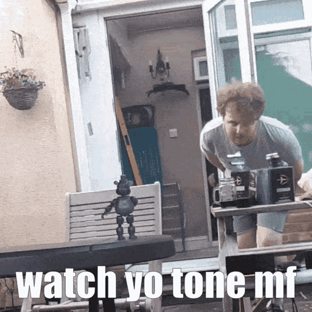 a man standing in front of a table with the words watch yo tone mf written below him