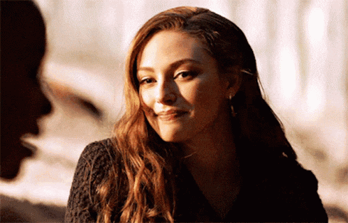 a woman with long red hair is smiling and looking at the camera while sitting next to a man .