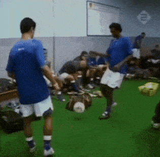 a man in a blue shirt is kicking a soccer ball in a locker room