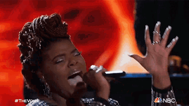 a woman singing into a microphone with nbc written on the bottom right