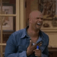 a bald man in a denim shirt is laughing while holding a broom .