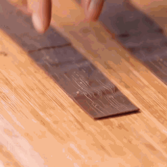 a person is holding a piece of chocolate on a wooden surface