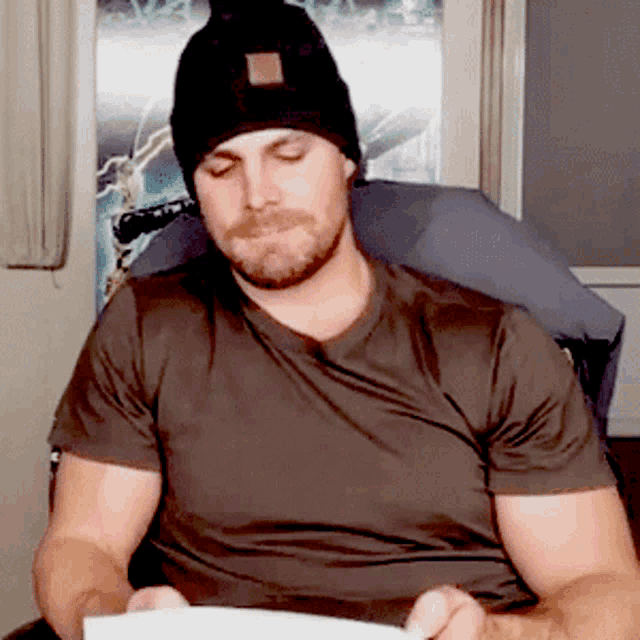 a man wearing a black beanie is reading a piece of paper