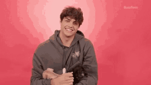 a young man in a gray hoodie is holding a cat in his arms .