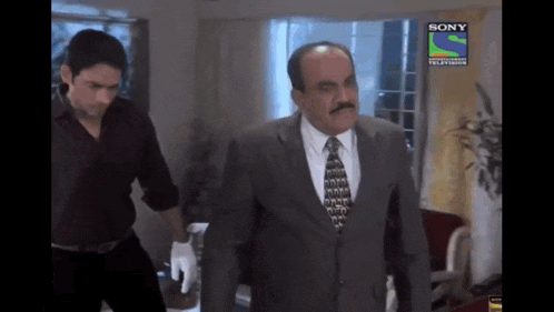 a man in a suit and tie is being escorted by a man in a black shirt by a sony television ad