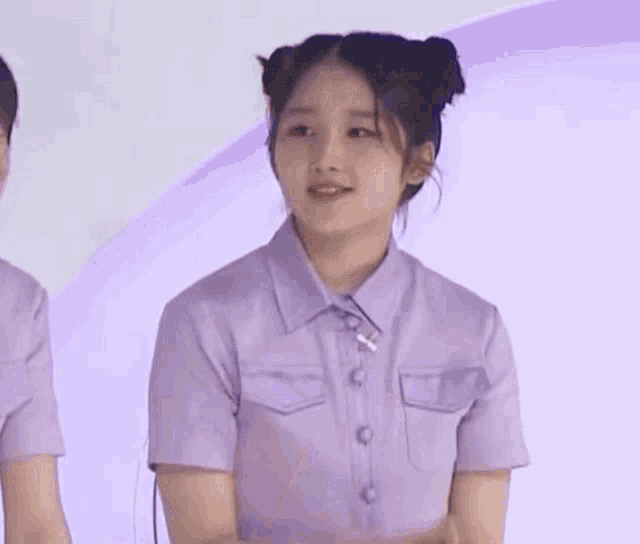 a girl in a purple shirt with two buns on her hair is making a funny face .