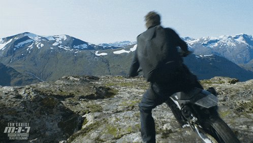 a man riding a motorcycle on top of a mountain with mountains in the background and tom cruise m.i.7 on the bottom