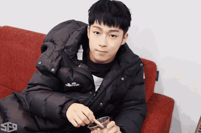 a young man in a black jacket is sitting on a couch