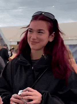 a woman with red hair is wearing sunglasses and holding a can of beer .