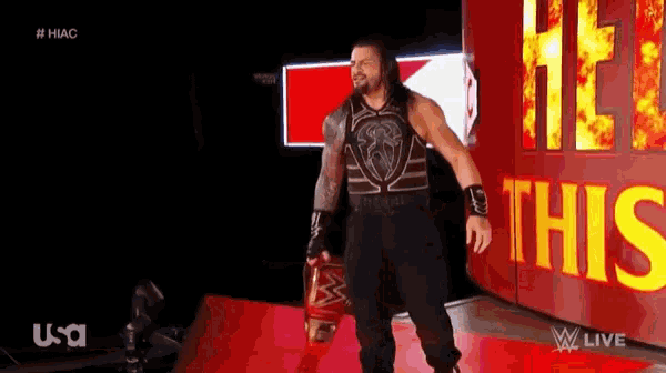 roman reigns is walking on a red carpet holding a wrestling championship belt .
