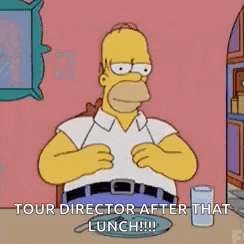 homer simpson is sitting at a table eating a plate of food .