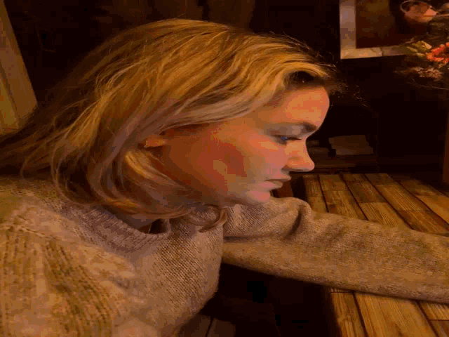 a woman in a grey sweater is laying down with her head down