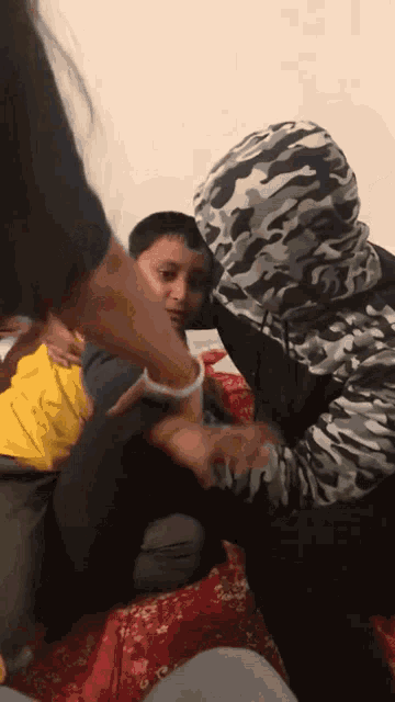 a man wearing a camouflage hoodie is holding a child 's arm