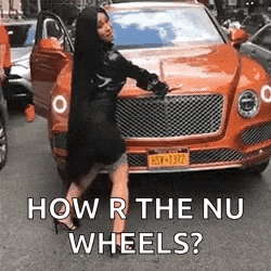 a woman in a black dress is standing next to an orange bentley car .
