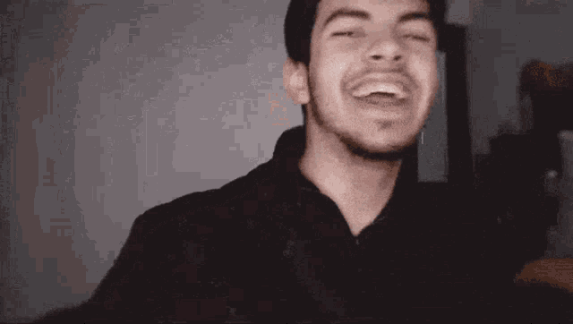 a man with a beard is laughing with his mouth open in a room .