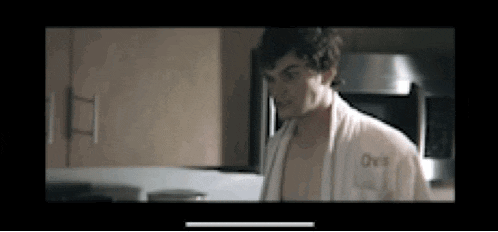 a shirtless man is standing in a kitchen wearing a robe .