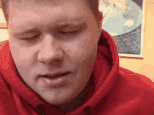 a man wearing a red hoodie looks down with his eyes closed