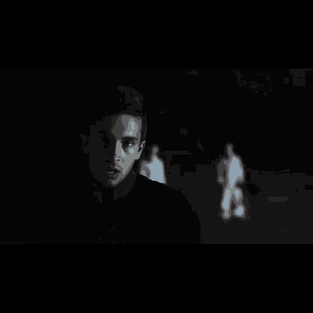 a man in a black shirt is standing in a dark room with a ghost in the background .