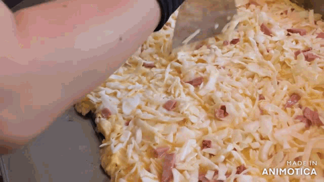 a person is spreading cheese on a pizza with ham .