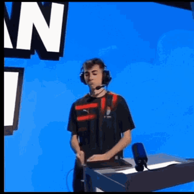a young man wearing headphones and a microphone is standing in front of a blue background .