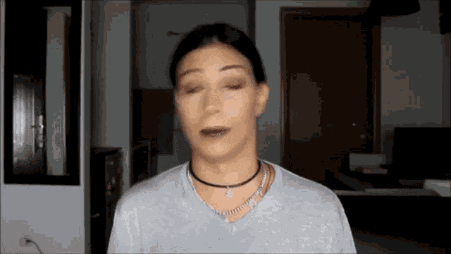 a woman is wearing a choker necklace and a gray shirt .
