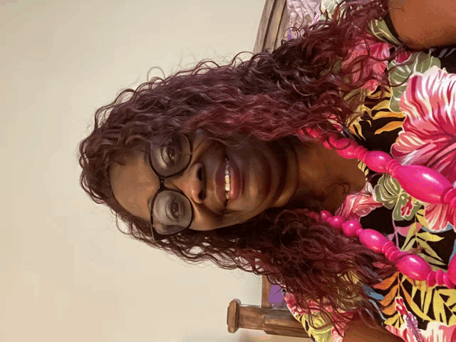 a woman with curly red hair wearing glasses and a pink necklace