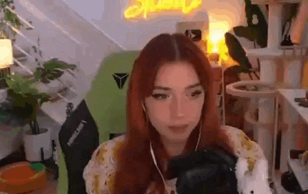 a woman with red hair is sitting in a green chair in a room with a cat tree .