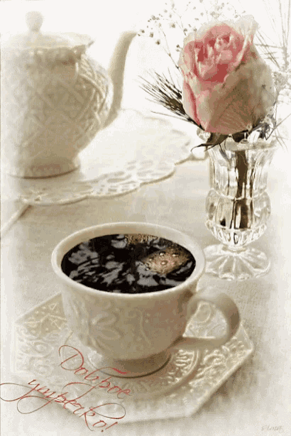 a cup of coffee sits on a saucer next to a pink rose in a vase