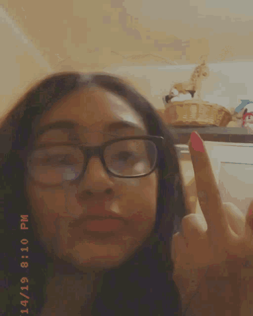 a girl wearing glasses is giving the middle finger and the time is 8:10 pm
