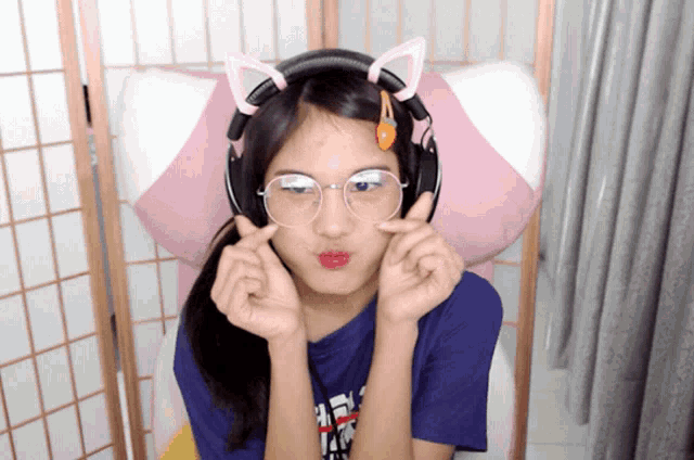 a girl wearing headphones and glasses makes a heart with her hands