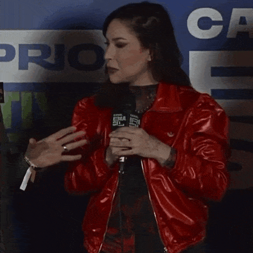 a woman in a red jacket is talking into a microphone in front of a sign that says prior