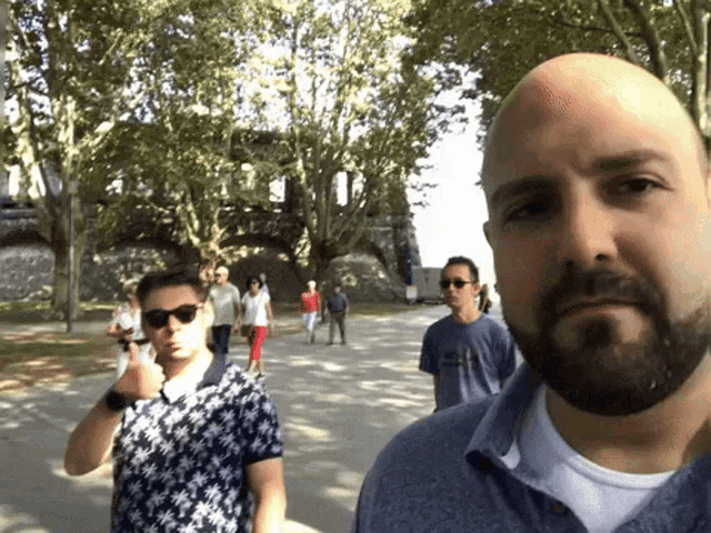 a bald man with a beard and sunglasses stands in a park