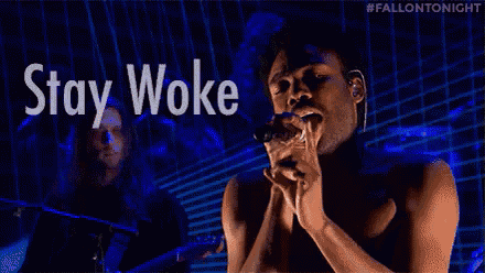 a man is singing into a microphone with the words stay woke behind him