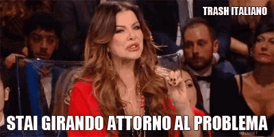a woman in a red jacket stands in front of a crowd and says " stai girando attorno al problema " .