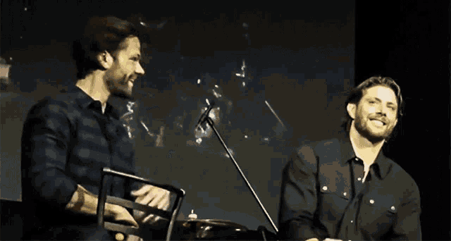 two men are laughing on a stage and one of them is wearing a black shirt