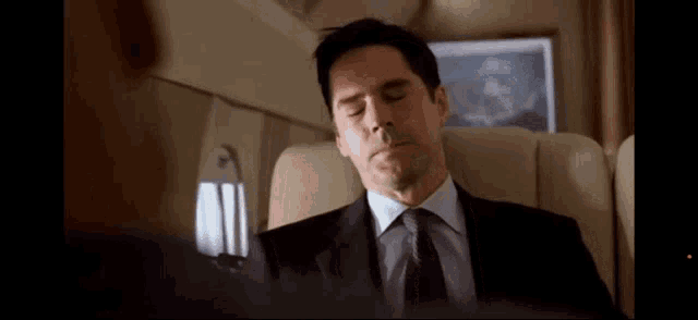 a man in a suit and tie sleeping on a plane