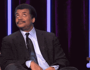 a man in a suit and tie is sitting on a stage with the words `` just kidding '' written on the screen .